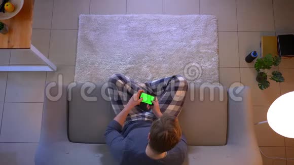 特写镜头年轻的穿着随意的男性在手机上玩电子游戏而坐在沙发上视频的预览图