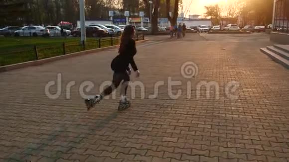 一个滑旱冰的女孩骑着她的背对着镜头在一个城市的街道上视频的预览图