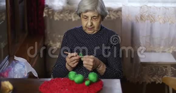 头发灰白皱纹深的老妇人用绿色的线编织视频的预览图