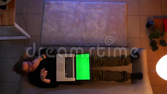 在沙发上躺着的绿色屏幕上美丽的女性在笔记本电脑上发短信的特写镜头视频的预览图