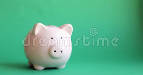 男人把硬币放在绿色背景上猪形的储蓄罐里视频的预览图