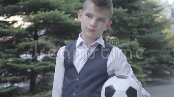 肖像可爱的衣冠楚楚的男孩站在街上拿着足球和钱包严肃的年轻人视频的预览图
