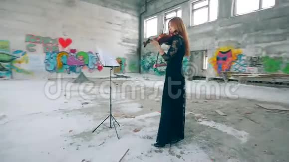 一位女士正在一座空楼里拉小提琴里面有涂鸦墙视频的预览图