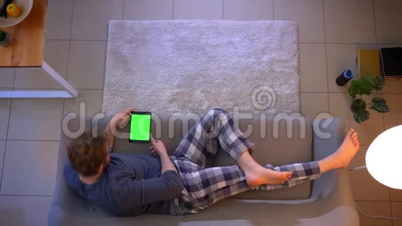 年轻的穿着随意的男性躺在平板电脑上看广告的特写镜头视频的预览图