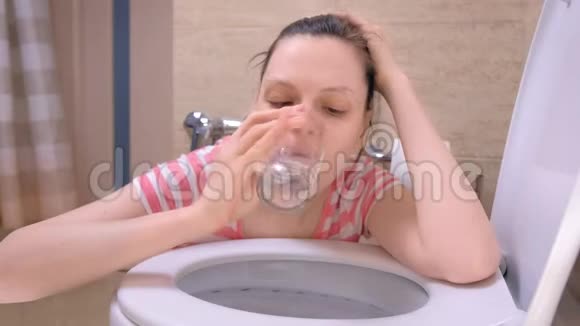 年轻的患病妇女在厕所呕吐坐在地板上手里拿着水玻璃食物中毒症状视频的预览图