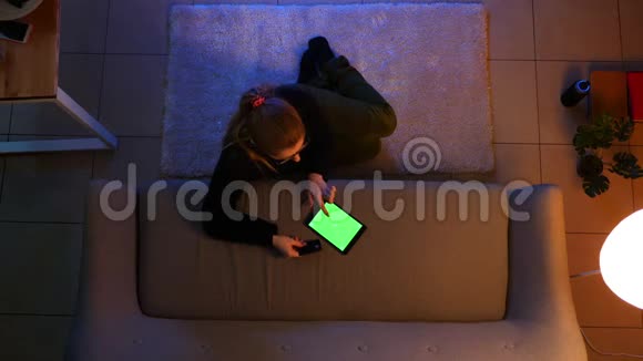在舒适的公寓里一个漂亮的女孩子坐在地板上用平板电脑拍摄特写镜头视频的预览图