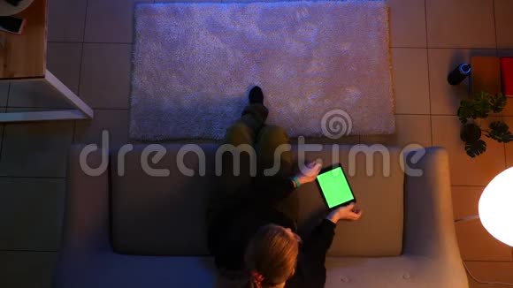 坐在沙发上使用平板电脑绿色屏幕和冲浪社交媒体的漂亮女性特写镜头视频的预览图