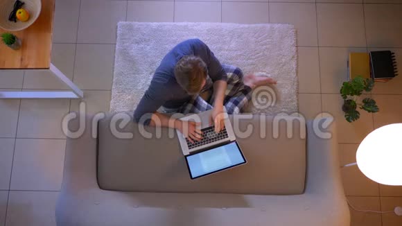 年轻的穿着随意的男性在网上学习并在坐在地上的笔记本上写一篇文章的特写镜头视频的预览图