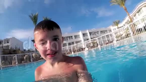 带着滑稽脸的快乐男孩在游泳池的自拍相机上拍摄了一段自己的视频视频的预览图
