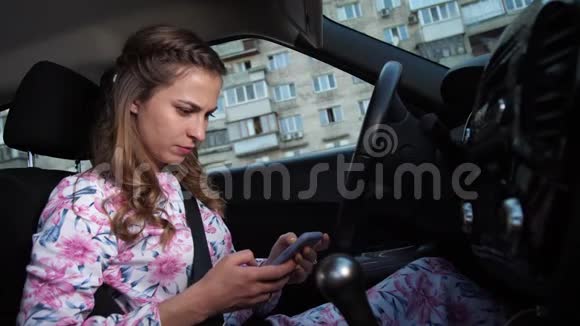 一个年轻的女孩坐在方向盘后面在电话上读到一些东西4K慢慢视频的预览图