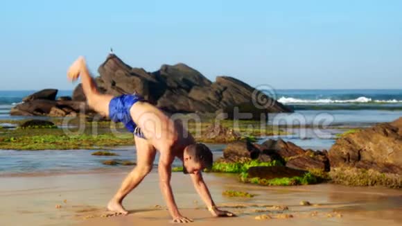 英俊的体操运动员在海岸潮湿的沙滩上双手行走视频的预览图
