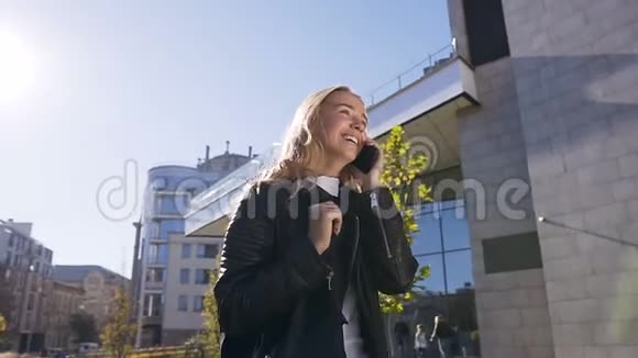 美丽的金发女孩在智能手机上说话在街上散步和享受城市生活时微笑的肖像视频的预览图