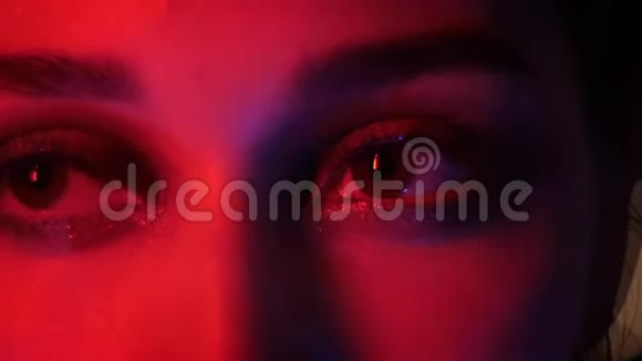 特写镜头漂亮的女性眼睛与诱人的时尚化妆红色霓虹灯和bokeh背景看着视频的预览图