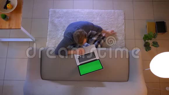 年轻时穿着随意的男性电脑打字特写镜头绿色屏幕坐在室内的地板上视频的预览图