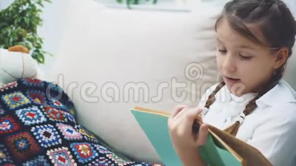 可爱的小女孩坐着双腿蜷曲为她的泰迪读童话故事有感情地移动她的手表现出视频的预览图