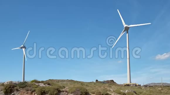 阳光明媚的一天两台风力涡轮机和山景之间的道路对角线拍摄视频的预览图