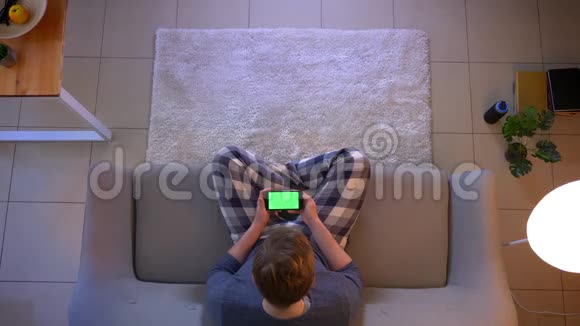 在舒适的家中一位穿着随意的年轻男性在手机上观看一则广告屏幕为绿色视频的预览图