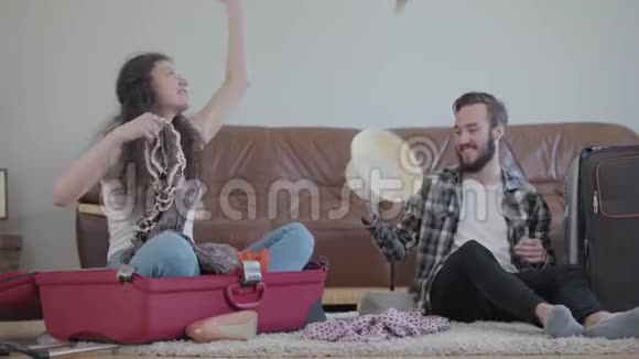 快乐男女在家门口地板上的皮沙发前整理旅行前的行李箱妻子扔了视频的预览图