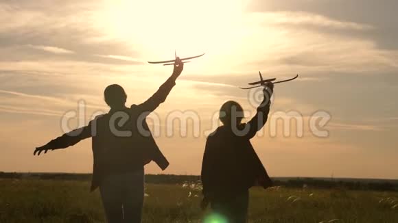 孩子们手里拿着一架飞机在太阳的背景下发呆两个女孩在日落时玩玩具飞机剪影视频的预览图
