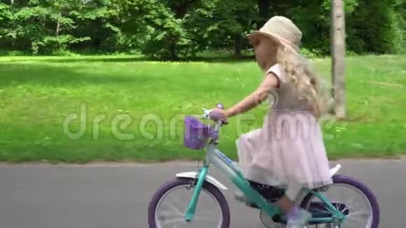 可爱的白人女孩带帽子骑自行车在城市公园万向节运动视频的预览图