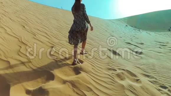 年轻的美女穿着长裙沿着迪拜沙漠的沙丘漫步视频的预览图