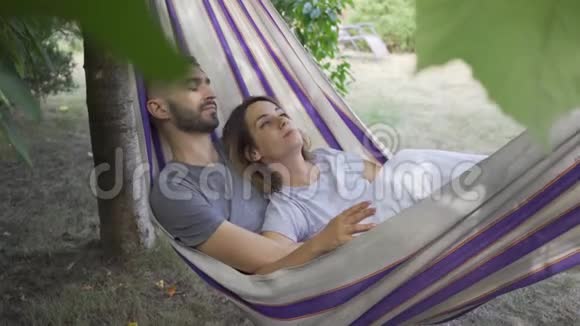 年轻的白种人男女躺在花园的吊床上一起放松爱的情侣一起在户外视频的预览图