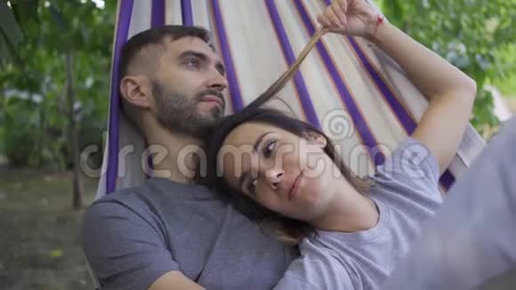快乐的年轻白种人男女躺在吊床上一起放松爱的情侣一起在户外视频的预览图