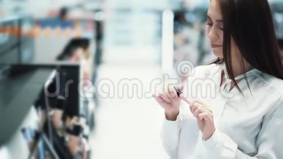 年轻漂亮的女人在化妆品店里选择口红试着涂在嘴唇上视频的预览图