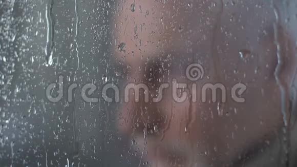 悲伤的老人看着窗外的雨天思索着自己的人生特写视频的预览图