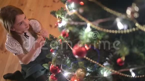 一个可爱的女孩坐在房间的地板上欣赏和玩挂在圣诞树上的球视频的预览图