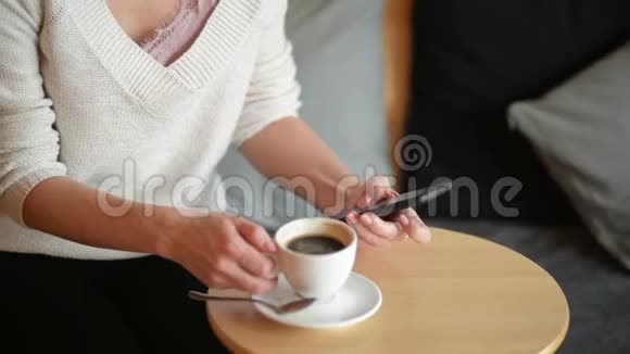 女人在桌子上写字喝咖啡或茶她搅拌着杯子看着智能手机特写视频的预览图