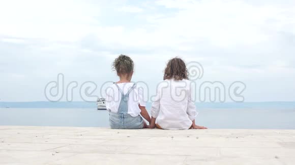 可爱的少女夫妇坐在海边孩子们互相看着女孩把头靠在男孩的肩上视频的预览图