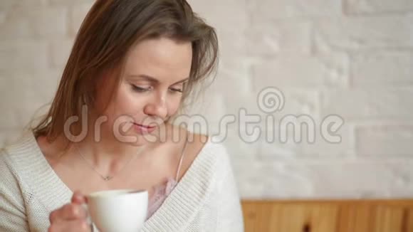女人在桌子上写字喝咖啡或茶她端着杯子看着智能手机特写视频的预览图