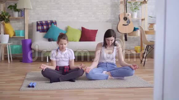 妈妈和女儿坐在地板上做瑜伽视频的预览图