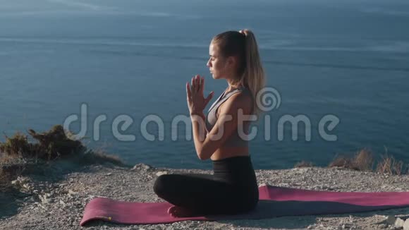 女人坐在垫子上的莲花瑜伽姿势在户外冥想慢动作视频的预览图