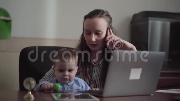 一幅忙碌的年轻母亲在家工作的肖像她的大腿上有婴儿3这个女人一边打手机一边说话视频的预览图