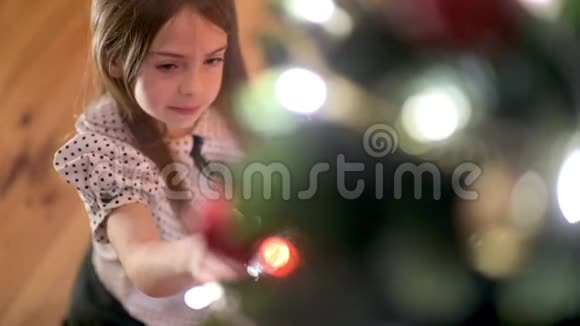 一个可爱的女孩坐在房间的地板上欣赏并玩挂在圣诞树上的球视频的预览图