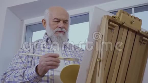 老人在靠近窗户的画架上画画视频的预览图