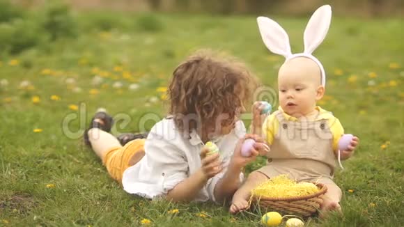 可爱的孩子们一个小学生和一个孩子坐在绿草上玩复活节彩蛋复活节篮子视频的预览图