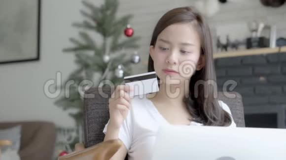美丽的肖像年轻的亚洲妇女在网上购物用笔记本电脑上网坐在家里的客厅里视频的预览图