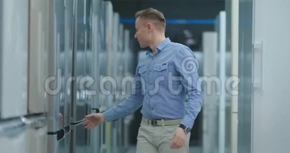 穿着蓝色衬衫的帅哥打开电器商店的冰箱门与其他模特比较买一台新的视频的预览图
