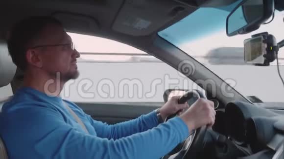 穿蓝色衬衫的白人驾驶汽车在智能手机上观看视频视频的预览图