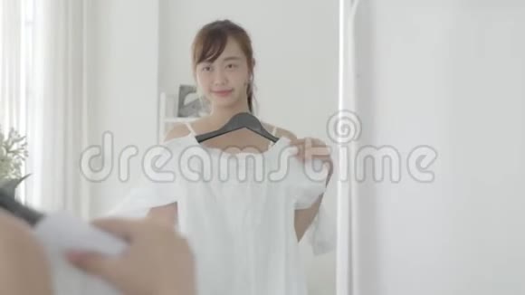 美丽的肖像亚洲年轻女子微笑着在卧室照镜子亚洲女孩试着穿衣服视频的预览图