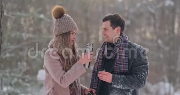 一个有爱心的男人在白雪覆盖的公园里的冬天温暖妻子的双手视频的预览图