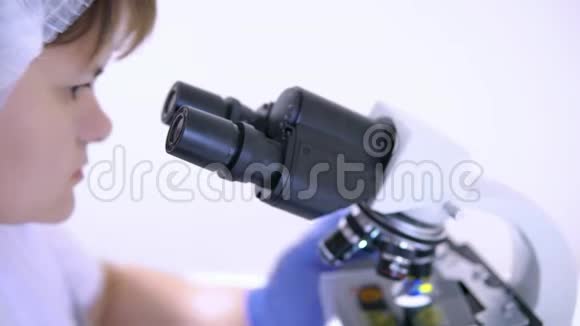 年轻女实验室技术员看着显微镜目镜的脸视频的预览图