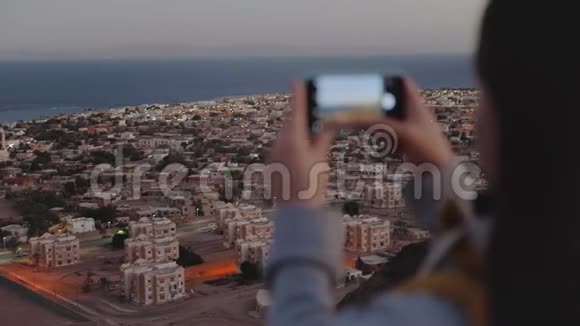 晚上女人用智能手机拍海女人呆在山顶眺望地平线视频的预览图