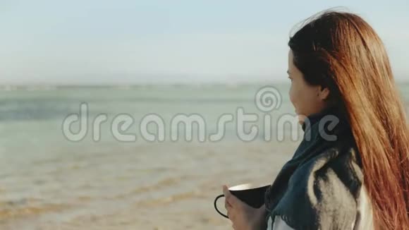 女人正在海滩上喝咖啡或茶海景蓝色女人看地平线快速视频慢动作4K视频的预览图