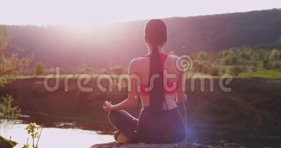 年轻的女士在大自然中和河流一起练习瑜伽她有一个冥想姿势视频的预览图