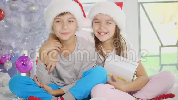 有趣的视频兄妹戴着圣诞帽温柔地拥抱分享圣诞礼物坐在白色的帽子上视频的预览图