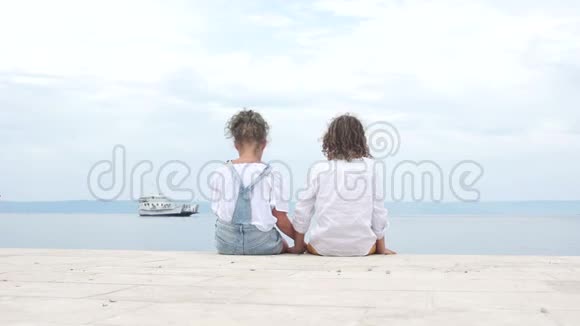 友好的孩子们手牵手坐在码头上男孩和女孩穿着夏天的白色衬衫和牛仔裤夏季视频的预览图